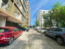 Parking area in front of buildings with various cars and trees