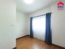 Minimalist bedroom with wooden floors, window, and blue curtains