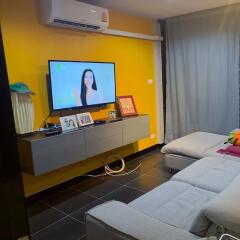 Modern living room with yellow accent wall, wall-mounted TV, and seating area