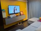 Modern living room with yellow accent wall, wall-mounted TV, and seating area