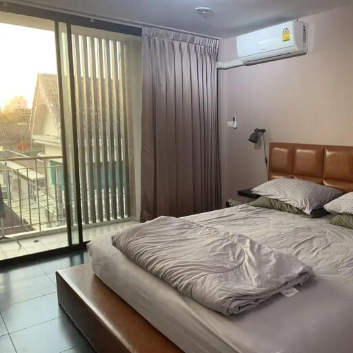 Bedroom with large sliding glass doors to a balcony, bed with brown leather headboard, air conditioner, and gray curtains