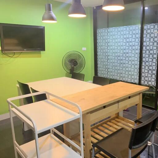 Modern dining area with green wall, table, chairs, TV, fan and pendant lights