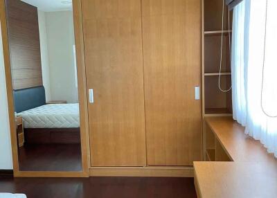 Bedroom with wooden furniture, a bed, wardrobe with mirror, desk, and window with white curtains