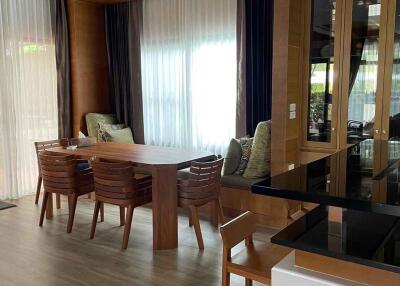 Modern dining area with wooden table and chairs, featuring large windows with curtains and built-in shelving.