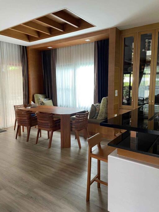 Modern dining area with wooden table and chairs, featuring large windows with curtains and built-in shelving.