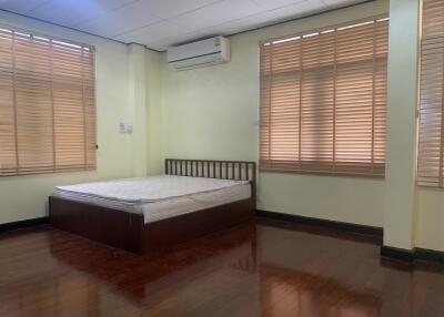 A bedroom with wooden floor, bed, large windows, and air conditioner