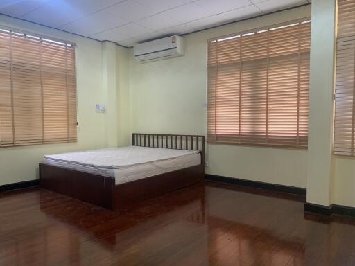 A bedroom with wooden floor, bed, large windows, and air conditioner