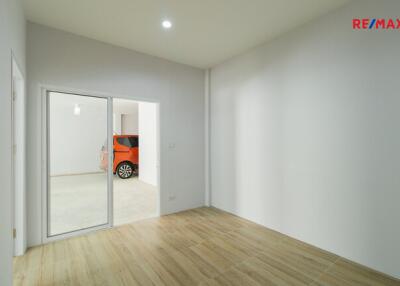 Vacant room with wooden flooring and a sliding glass door leading to a garage with an orange car