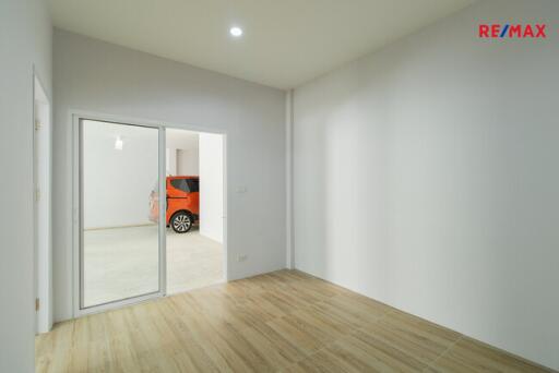 Vacant room with wooden flooring and a sliding glass door leading to a garage with an orange car