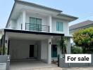 Exterior view of a two-story house with a carport and 'For Sale' sign