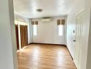 Empty bedroom with wooden floor, air conditioning unit, and two windows with blinds