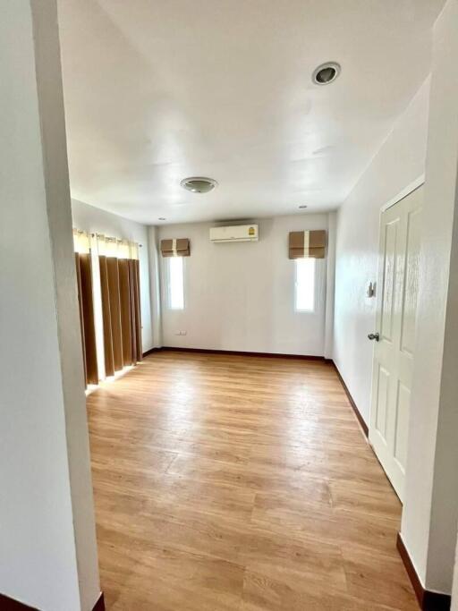Empty bedroom with wooden floor, air conditioning unit, and two windows with blinds