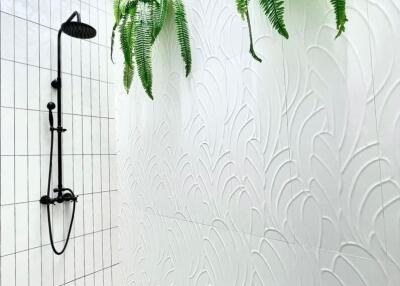 Outdoor shower area with black shower fixtures, white textured walls, decorative black and white tiles, and green plants