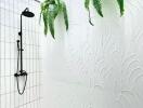 Outdoor shower area with black shower fixtures, white textured walls, decorative black and white tiles, and green plants