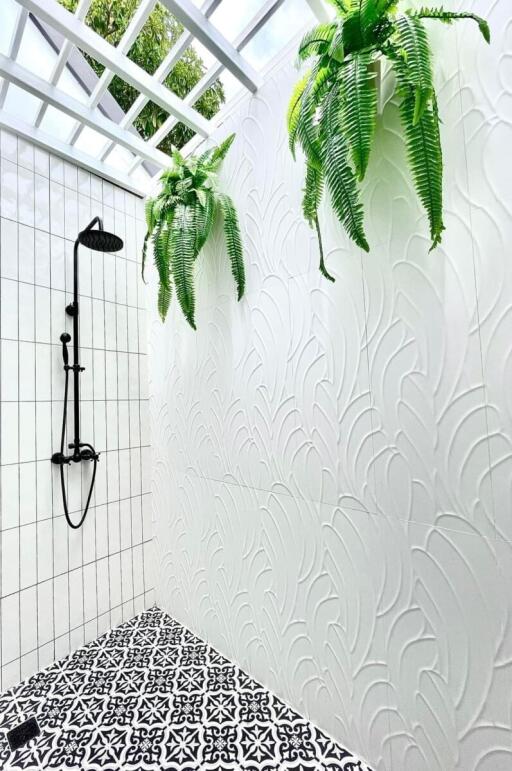 Outdoor shower area with black shower fixtures, white textured walls, decorative black and white tiles, and green plants