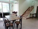 Dining area with metal chairs and table, adjacent to staircase and large glass windows.