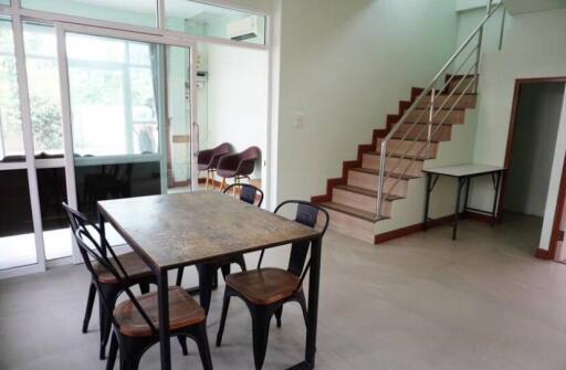 Dining area with metal chairs and table, adjacent to staircase and large glass windows.