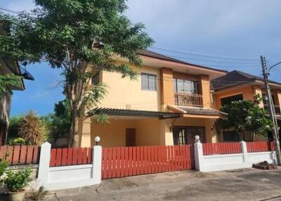 A two-story house with a red fence and a tree in the front yard