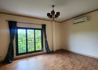 Empty living room with wooden flooring, a large window with green curtains, ceiling light fixture, and air conditioning unit.