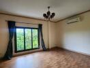 Empty living room with wooden flooring, a large window with green curtains, ceiling light fixture, and air conditioning unit.