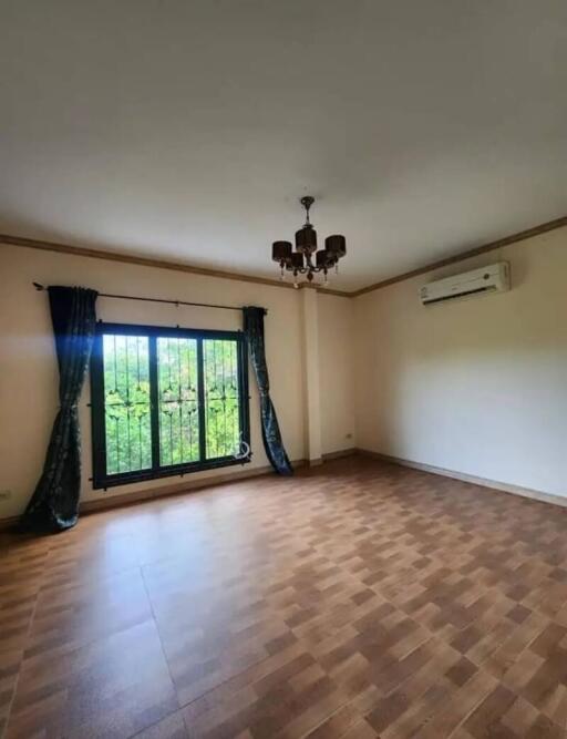 Empty living room with wooden flooring, a large window with green curtains, ceiling light fixture, and air conditioning unit.