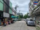 Street view showing buildings, vehicles, and nearby shops