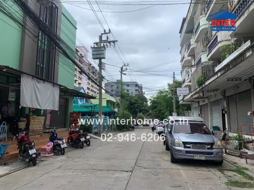 Street view showing buildings, vehicles, and nearby shops