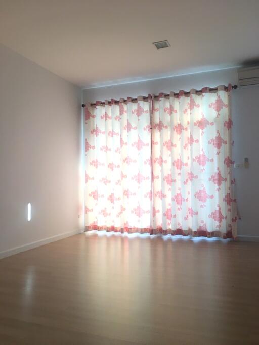 Spacious living room with wooden flooring and large window with floral curtains