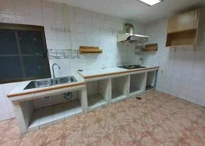 Empty kitchen with tiled surfaces, sink, and stove.