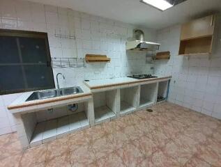 Empty kitchen with tiled surfaces, sink, and stove.