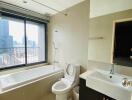 Modern bathroom with large window, bathtub, toilet, sink, and mirror