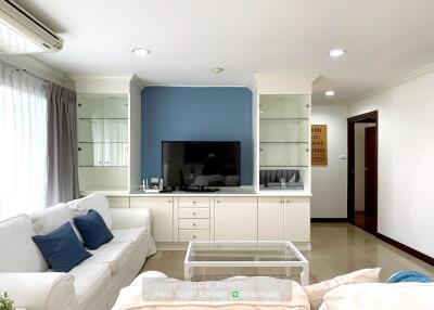 Well-lit living room with white sofas, blue accent wall, built-in storage, and flat-screen TV