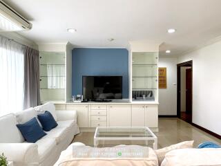 Well-lit living room with white sofas, blue accent wall, built-in storage, and flat-screen TV