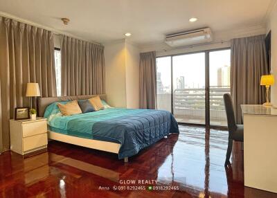 Bedroom with wooden floor, large bed, bedside tables, lamps, air conditioner, and balcony access.