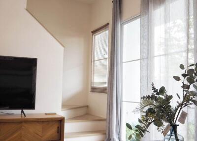 Modern living room with glass coffee table, wooden TV stand, large window, and staircase