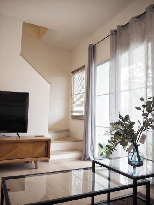 Modern living room with glass coffee table, wooden TV stand, large window, and staircase