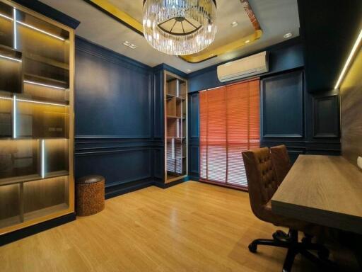 Modern home office with wooden flooring, built-in shelves, large desk, and chandelier lighting