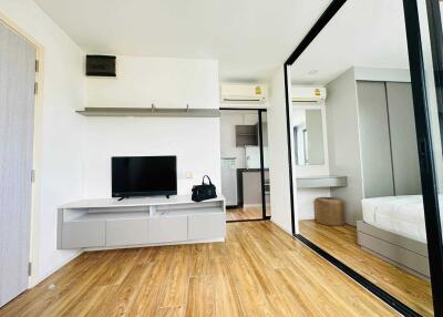 Modern living room with wooden floor, TV, shelves, and mirrored wardrobe