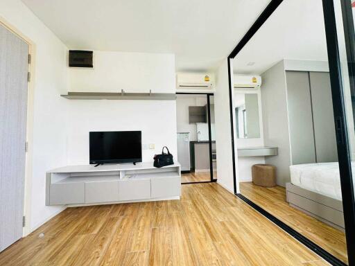 Modern living room with wooden floor, TV, shelves, and mirrored wardrobe