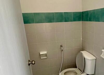 A small bathroom with a flush toilet, tiled walls and floor, and a bidet sprayer.