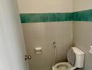 A small bathroom with a flush toilet, tiled walls and floor, and a bidet sprayer.