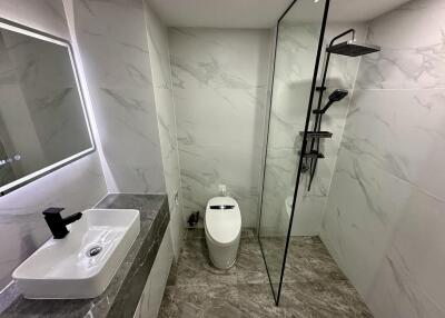 Modern bathroom with marble tiles, sink, toilet, and shower area