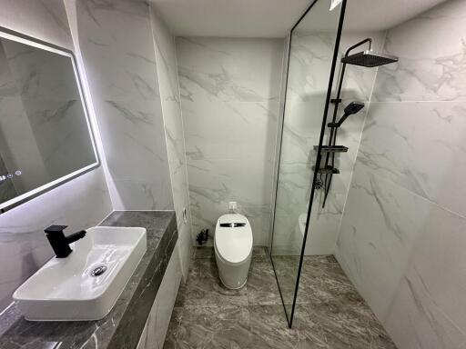 Modern bathroom with marble tiles, sink, toilet, and shower area