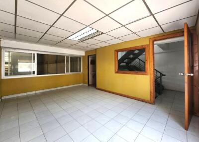 Spacious room with yellow walls, tiled floor, window, and wooden door, with adjacent room featuring staircase