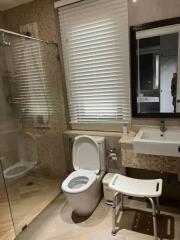 Modern bathroom with glass shower, toilet, sink, and seating stool