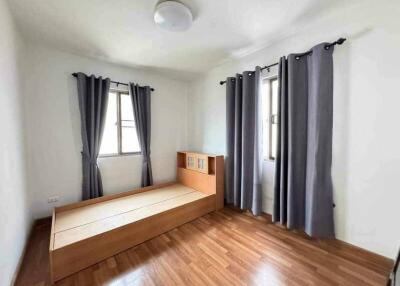 A bedroom with wooden flooring, a bed frame, and windows with grey curtains