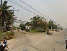 Street view of residential entrance with palm trees and motorbikes