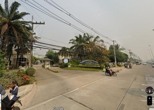Street view of residential entrance with palm trees and motorbikes