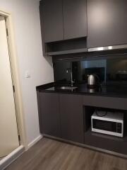 Modern kitchen with dark cabinets, sink, kettle, and microwave oven