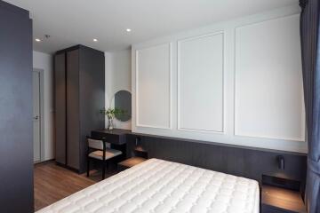 Modern bedroom with minimalistic design, featuring a bed, nightstands, a small desk, and a wardrobe